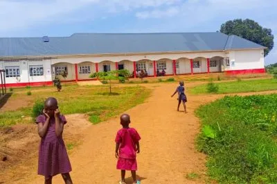 Kinder auf dem Weg zum langgestreckten Schulgebäude in Masaka, Uganda