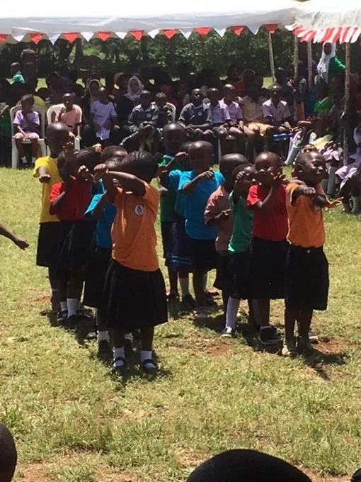 Schulkinder in Uniform versammeln sich auf einer Wiese, im Hintergrund bunte Wimpel